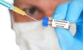 Man hand in blue nitrile glove hold small vial with coronavirus vaccine, to inject it with green orange syringe, blurred face with Royalty Free Stock Photo