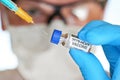 Man hand in blue nitrile glove hold small vial with coronavirus vaccine, to inject it with green orange syringe, blurred face with Royalty Free Stock Photo