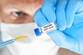 Man hand in blue nitrile glove hold small vial with coronavirus vaccine, to inject it with green orange syringe, blurred face with Royalty Free Stock Photo