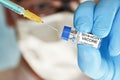 Man hand in blue nitrile glove hold small vial with coronavirus vaccine, to inject it with green orange syringe, blurred face Royalty Free Stock Photo