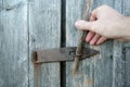 Man hand closes an old wooden door with a metal, rusty latch and stick, in a barn, outdoors. Royalty Free Stock Photo