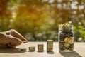 Man hand coins bar and jar on wooden table in sunlight and blur background present the Savings Coins - Investment And Interest and Royalty Free Stock Photo