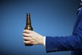 A man hand holding beer bottle on blue background. A hand holding up a beer bottle without label Royalty Free Stock Photo