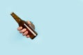 Man hand holding a bottle of beer through a hole in a light blue background Royalty Free Stock Photo