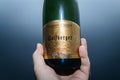 Man hand holding bottle of Cremant d`Alsace Wolfberger Demi-Sec sparkling wine against blue background