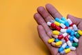 Man hand holding colorful capsule pills on yellow background. Prescription drugs. Drug overuse and polypharmacy concept. Drug