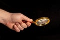 Man hand holding a gilded magnifying glass, close-up on black background. Copy space for your image or text Royalty Free Stock Photo