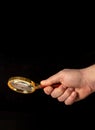 Man hand holding a gilded magnifying glass, close-up on black background. Copy space for your image or text Royalty Free Stock Photo