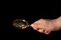 Man hand holding a gilded magnifying glass, close-up on black background. Copy space for your image or text Royalty Free Stock Photo