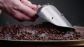 Man hand holding ladle scooping coffee seeds close up. Smoke coming from beans.