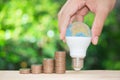 Man hand is holding the LED bulb as a globe site of the growing coins stack with green nature background for concept of saving Royalty Free Stock Photo