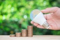 Man hand is holding the LED bulb as a globe site of the growing coins stack with green nature background for concept of saving Royalty Free Stock Photo