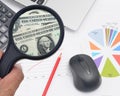 Man hand holding magnifying glass to see US dollar banknotes on spreadsheet and charts graphs paper. Royalty Free Stock Photo