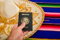 Man hand holding Mexican passport and mariachi hat on colorful serape.