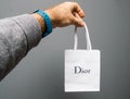 Man hand holding new gift from Christian Dior white paper bag against gray background Royalty Free Stock Photo