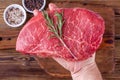 Man Hand Holding a Raw Fresh Beef Steak with Rosemary above a Cups with Herbs Royalty Free Stock Photo