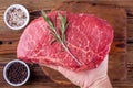 Man Hand Holding a Raw Fresh Steak with Rosemary above a Cups with Herbs Royalty Free Stock Photo