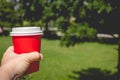 Man hand holding red coffee paper cup, lifestyle summertime shot.