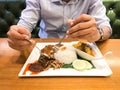 An asian man holding spoon and fork, eating set of delicious of chicken curry rice with fish chili sambal