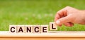 Man hand holding wooden cube block with CANCEL business word on green lawn background. Truth, beliefs and agreement