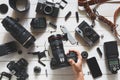 Man hand Holds Digital Camera On Table Next To Lenses And Accessories On White Wooden Background. Top View Royalty Free Stock Photo