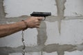 Man hand holds gun and ready to shoot on a grey wall background. Opened handcuffs hanging on a hand. copy space Royalty Free Stock Photo
