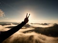 Man hand make victory to Sun. Misty daybreak in mountains