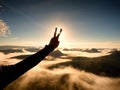 Man hand make victory to Sun. Misty daybreak in mountains