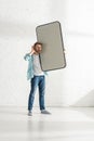 Man with hand near ear holding big model of smartphone near white brick wall Royalty Free Stock Photo