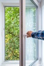 Man hand opens a PVC window from which you can see a tree in an ecologically clean area of the city, with fresh air. Royalty Free Stock Photo