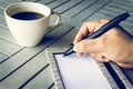 Man hand with pen writing on notebook. Coffee and notebook on wooden table. Royalty Free Stock Photo