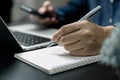 Man hand with pen writing on notebook with computer laptop at desk Royalty Free Stock Photo