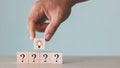 Man hand picked wooden cube block with light bulb icon overhead and question marks icons on table. Royalty Free Stock Photo