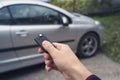 Man hand presses a button on the car remote control against blur car. New owner of a vehicle unlocks the purchase