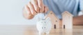 Man hand put coin into White piggy bank with wooden house on wood table. saving money for buying house, financial plan home loan Royalty Free Stock Photo