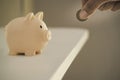 man hand putting money coin into the piggy bank on a white wooden office desk