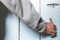 Man hand in a shirt closes a wooden door with a latch, painted blue, in a farmhouse.