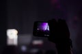 Man hand with a smartphone records a live concert of the group consisting of four cellists and a drummer. The scene is lit with Royalty Free Stock Photo