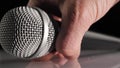 Man hand takes a cardioid microphone in his hand from a white table against black background. Concept of stay at home