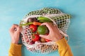 Man hand taking peach fruit from mesh shopping bag with fruits and vegetables. Eco friendly shopping