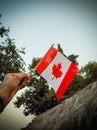 Man hand waving Canada flag against the sky close-up. Guy holding Canadian flag and celebrating national Canada day on 1st july Royalty Free Stock Photo