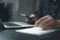 Man hand is writing on a notepad with a pen and a smart phone on desk Royalty Free Stock Photo