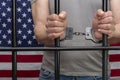 A man is handcuffed in a cell behind bars against the background of an American flag. Concept: the prisoner in the courtroom, the Royalty Free Stock Photo