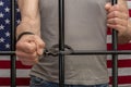 A man is handcuffed in a cell behind bars against the background of an American flag. Concept: the prisoner in the courtroom, the Royalty Free Stock Photo