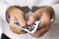 A man in handcuffs holds a sheet with a barcode, the concept of punishment for forgery of QR codes