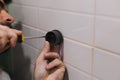 Man hands attaching plastic component of shower head holder to tiled wall in washroom with screwdriver with part of face Royalty Free Stock Photo