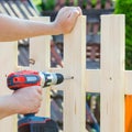 Man hands building wooden fence with a drill and screw. DIY concept. Close up of his hand and tool.