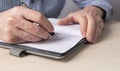 Man hands closeup taking notes in planner. Man sitting at table in office or at home, working or studying and writing