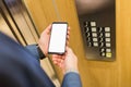 Man hands holding blank screen mobile phone next to elevator control panel