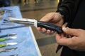 Man hands holding a handmade knife in front of a counter with knives, exhibition